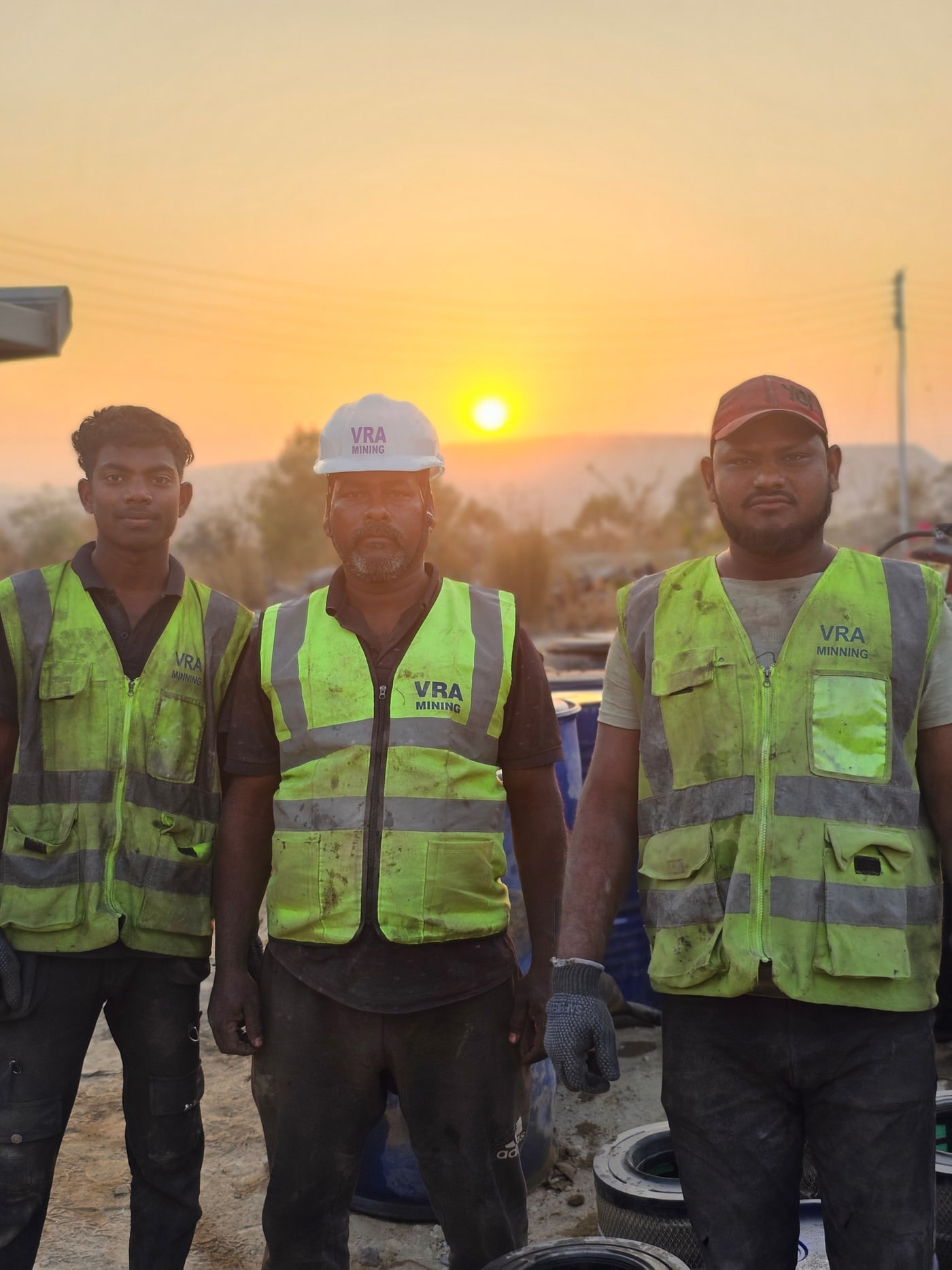 Three VRA technicians in hi-vis vests and hard hats at the mine face at sunset