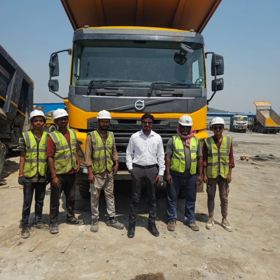 VRA On-Site Team wearing safety vests and white hard hats standing in front of a yellow Volvo dump truck